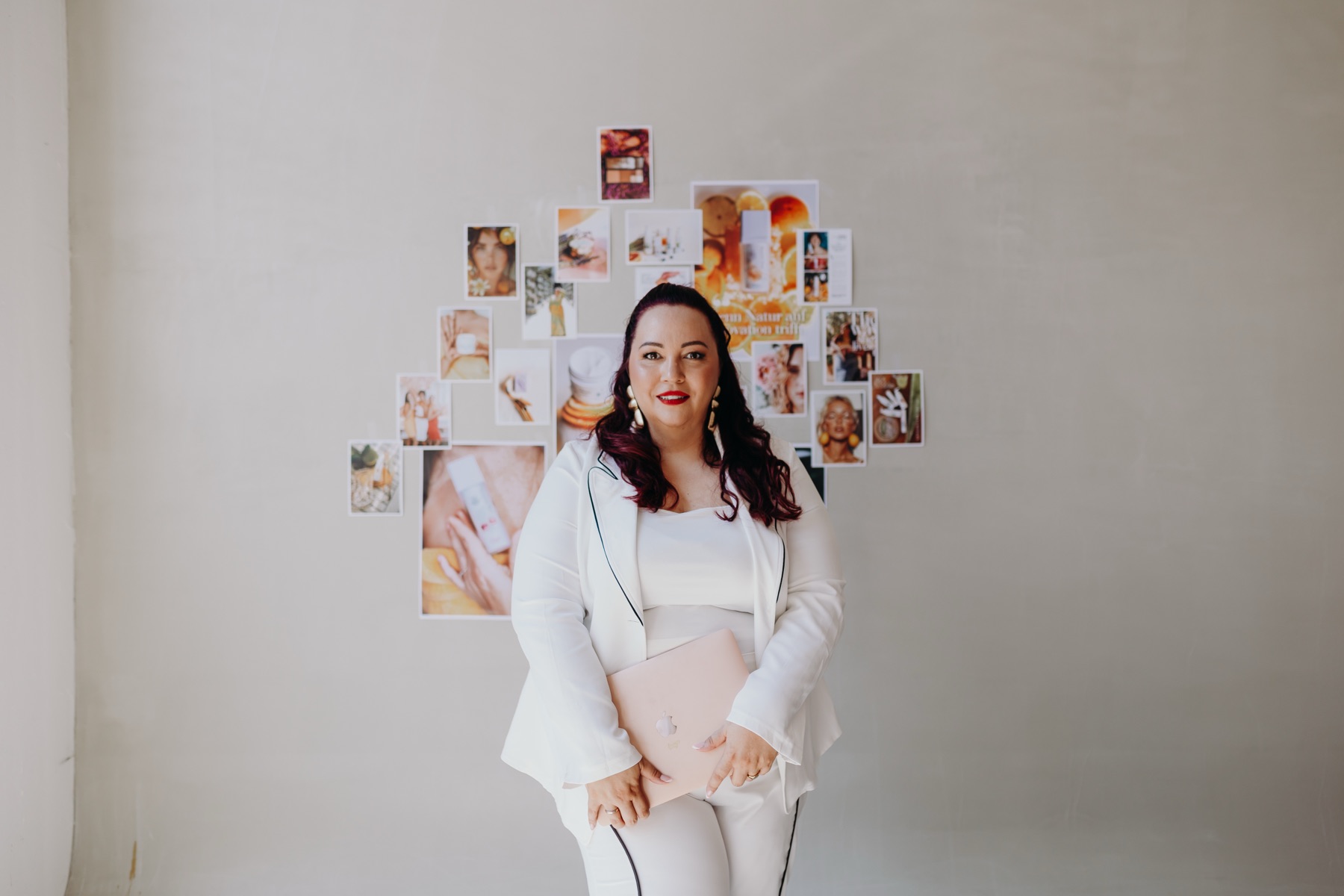 Nadine Kluge in Weiß vor einem Moodboard mit Beauty-Motiven, Ordner im Arm
