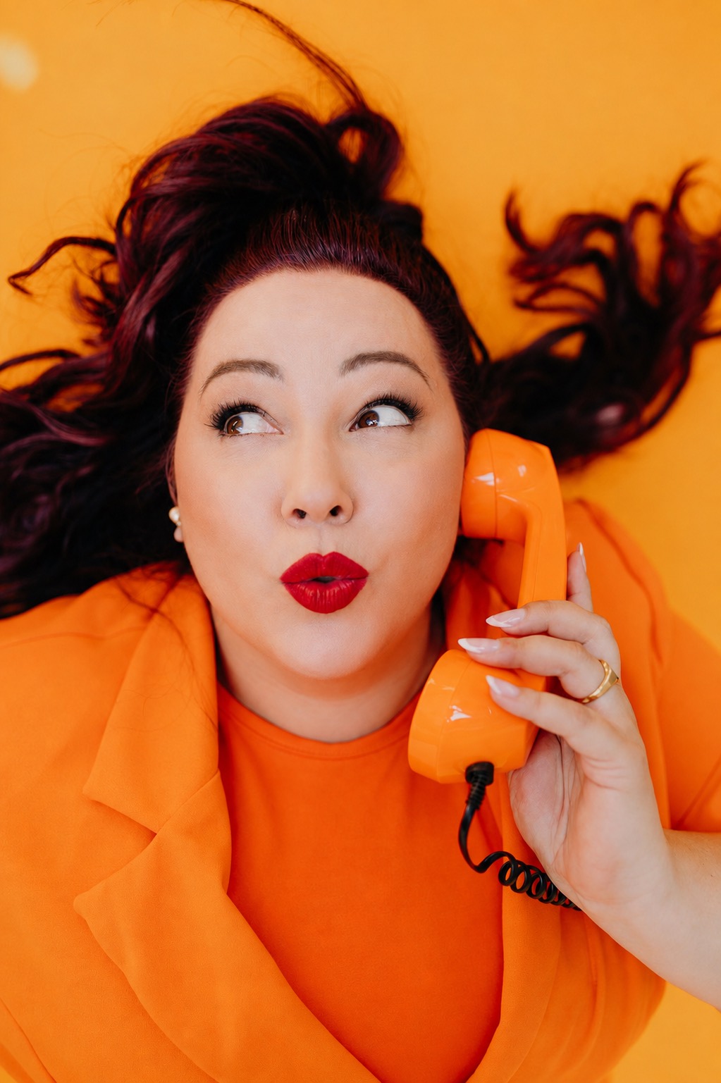 Nadine Kluge im orangen Anzug, lachend am orangen Telefon